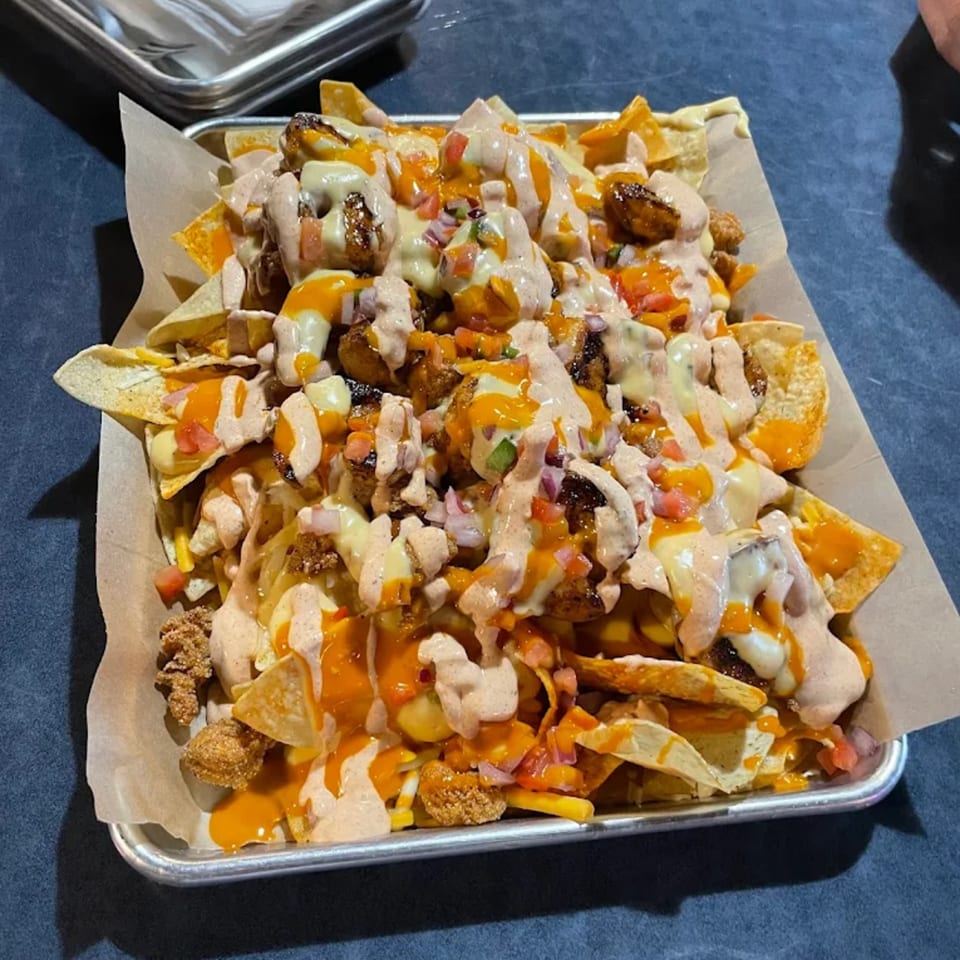 A tray of Bayou Cajun Smokehouse nachos with melted cheese, sauce, and toppings.