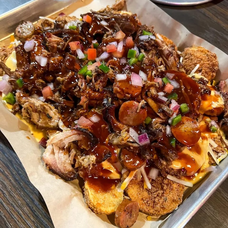 A tray of loaded Cajun nachos with pulled pork, sausage, cheese sauce, and diced vegetables.