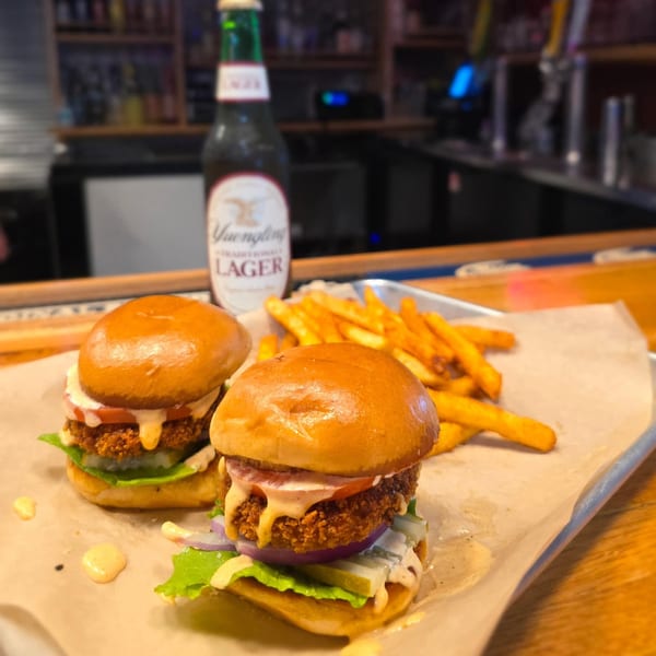 Two crispy chicken sliders with fries and a Yuengling beer bottle on a bar top.