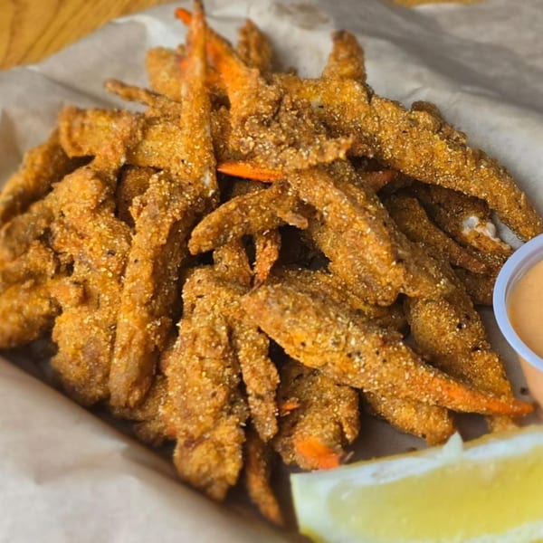 Fried crab claws, seasoned and breaded, with a side of sauce and a lemon wedge.