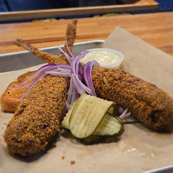 Three fried alligator tails with red onion, pickles, and a side of dipping sauce.