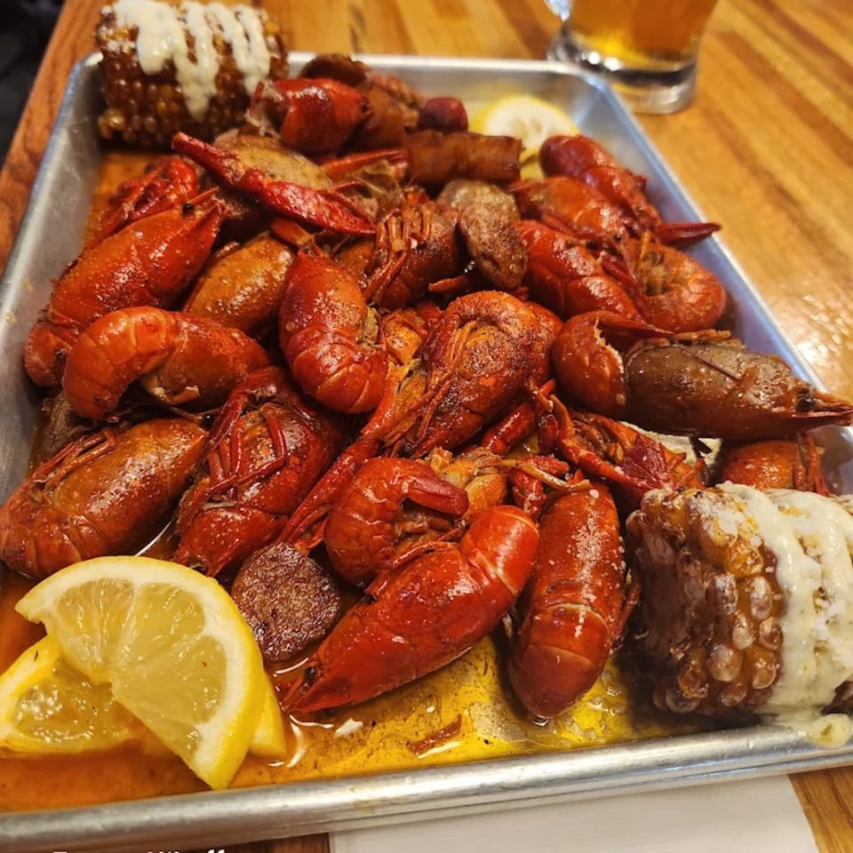A metal tray filled with bright red Cajun crawfish, corn on the cob, and lemon wedges.